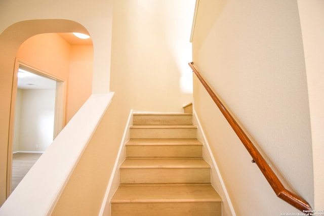 stairs featuring arched walkways and wood finished floors