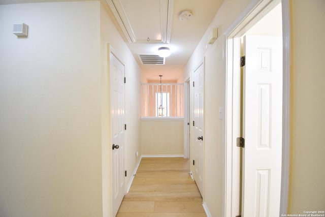 hallway with attic access, visible vents, light wood-style flooring, and baseboards