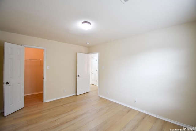 unfurnished bedroom featuring light wood-style flooring, baseboards, and a spacious closet