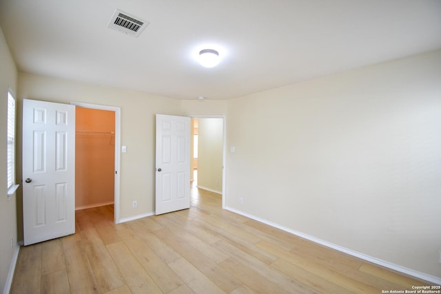 unfurnished bedroom featuring visible vents, baseboards, light wood-style floors, a closet, and a walk in closet