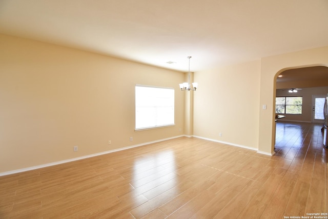 unfurnished room featuring arched walkways, light wood finished floors, and baseboards