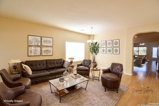 living room featuring light wood-style floors, baseboards, arched walkways, and a notable chandelier