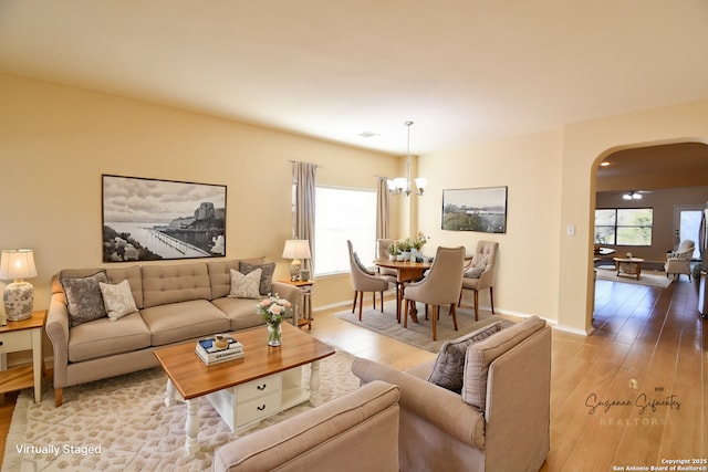 living area with arched walkways, a healthy amount of sunlight, light wood-style flooring, and baseboards