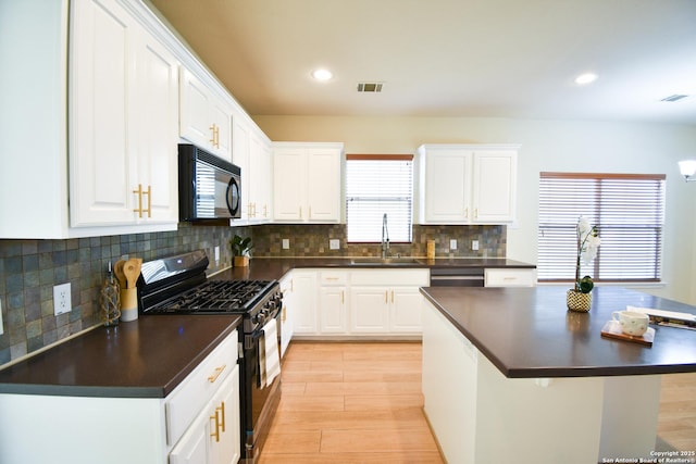 kitchen featuring black microwave, dark countertops, white cabinetry, and range with gas stovetop