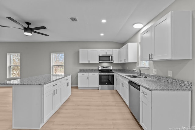 kitchen with light stone counters, stainless steel appliances, visible vents, white cabinetry, and a sink