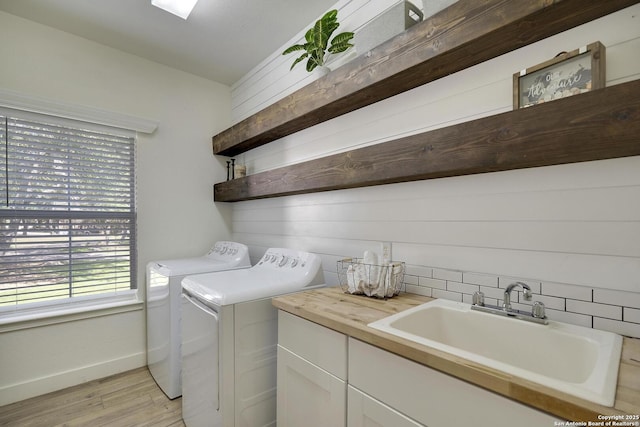 laundry area featuring cabinet space, light wood finished floors, baseboards, washing machine and clothes dryer, and a sink