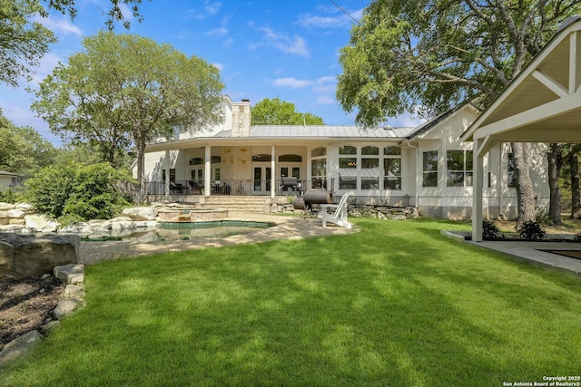 back of property featuring a lawn, a patio, a chimney, metal roof, and a standing seam roof