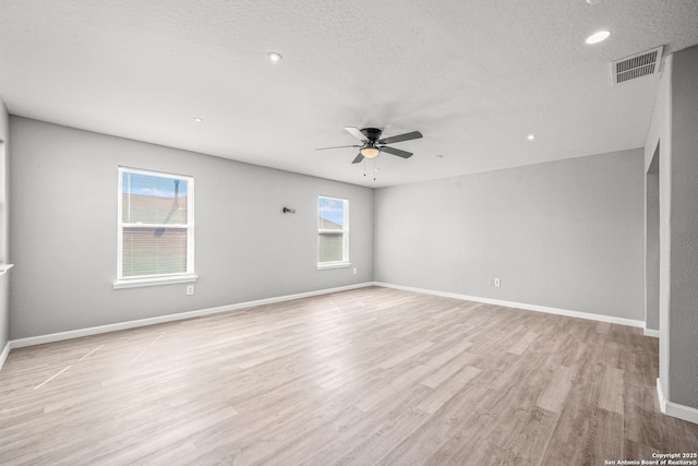 unfurnished room with a textured ceiling, light wood-type flooring, visible vents, and baseboards