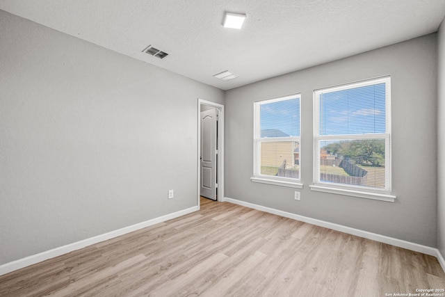 unfurnished room with light wood-style floors, visible vents, a textured ceiling, and baseboards