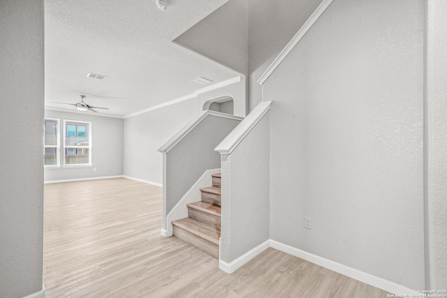 stairs featuring crown molding, visible vents, a textured ceiling, wood finished floors, and baseboards