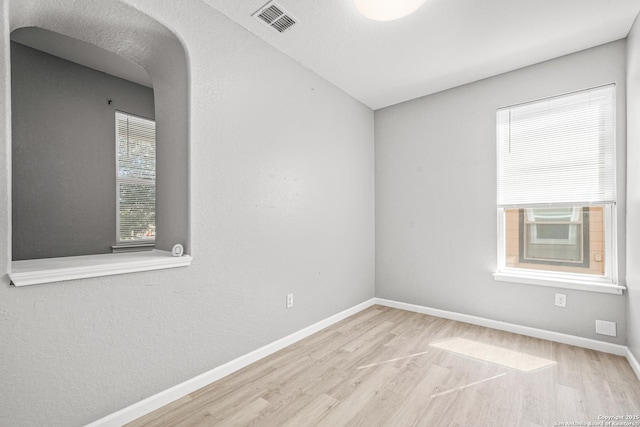 empty room featuring arched walkways, light wood finished floors, visible vents, and baseboards