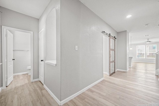 hall with a barn door, light wood-type flooring, and baseboards