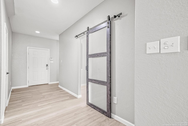 interior space with baseboards, a textured wall, a barn door, and light wood-style floors