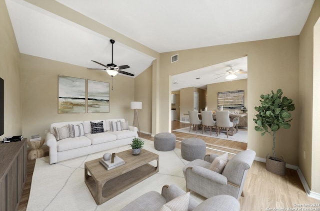 living area with a ceiling fan, visible vents, vaulted ceiling, baseboards, and light wood-type flooring