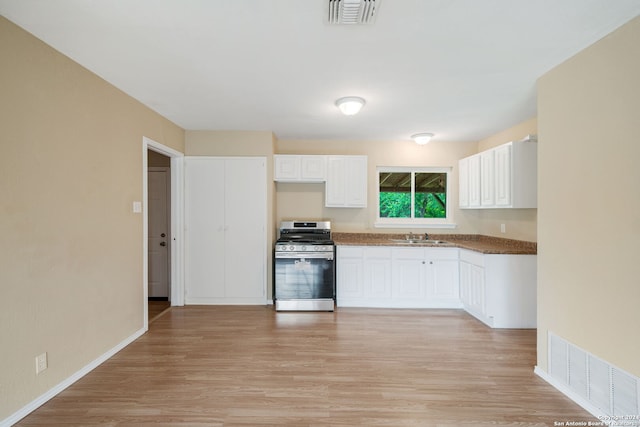 kitchen with light wood-type flooring, stainless steel range with gas cooktop, visible vents, and white cabinets