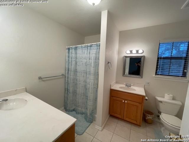 bathroom with toilet, curtained shower, tile patterned flooring, and vanity