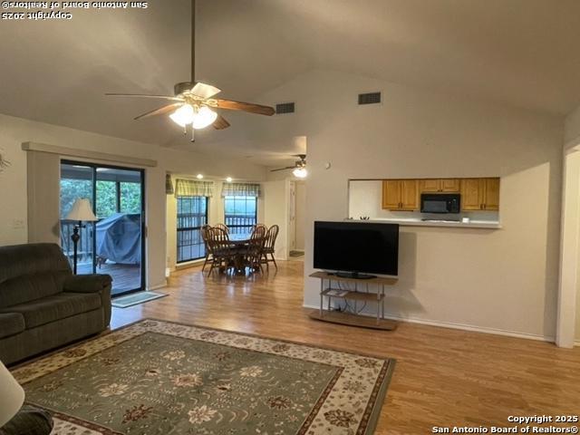 living area with light wood-style floors, visible vents, high vaulted ceiling, and a ceiling fan