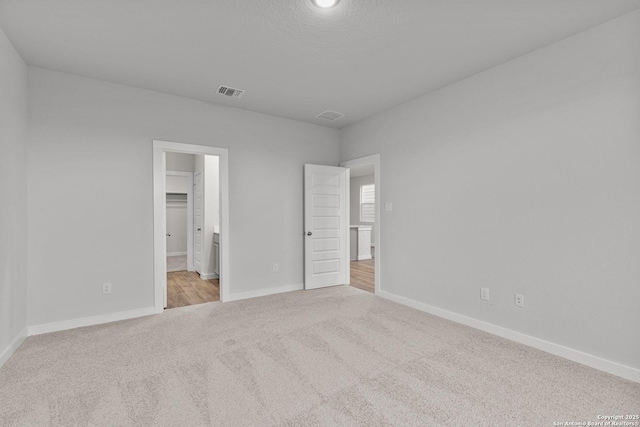 unfurnished bedroom featuring light carpet, ensuite bath, baseboards, and visible vents