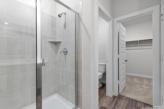 full bath featuring toilet, a stall shower, a walk in closet, and wood finished floors