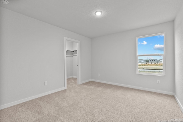 unfurnished bedroom featuring a closet, a spacious closet, light carpet, a textured ceiling, and baseboards