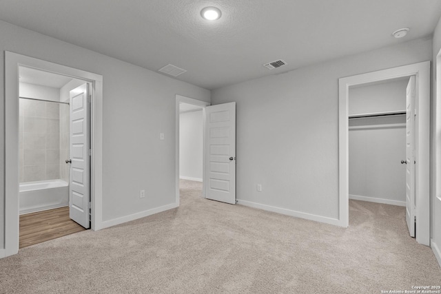 unfurnished bedroom with light carpet, baseboards, visible vents, a spacious closet, and a textured ceiling