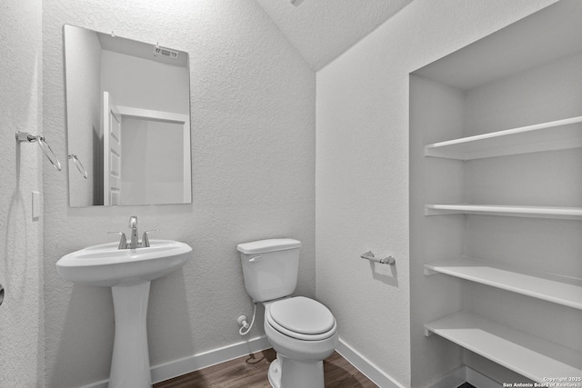 bathroom with baseboards, a textured wall, toilet, wood finished floors, and a sink