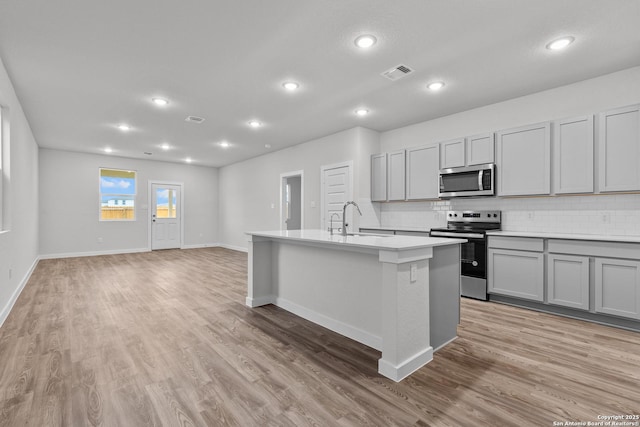 kitchen with stainless steel appliances, a sink, visible vents, light countertops, and an island with sink