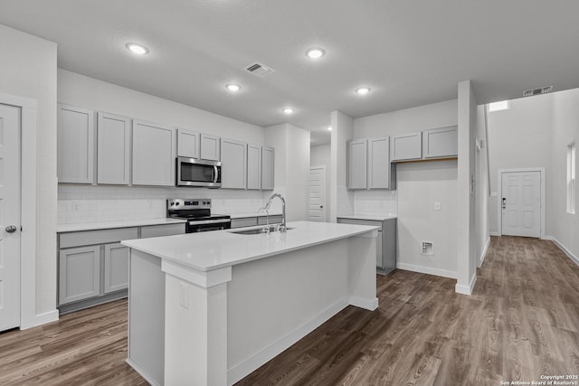 kitchen with stainless steel appliances, light countertops, gray cabinetry, a kitchen island with sink, and a sink