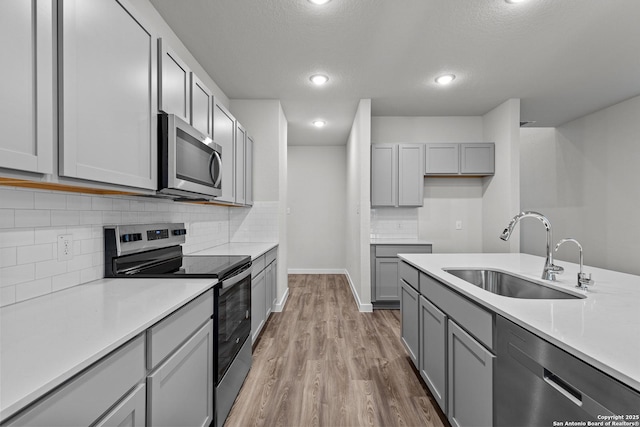 kitchen with gray cabinets, stainless steel appliances, light countertops, light wood-type flooring, and a sink