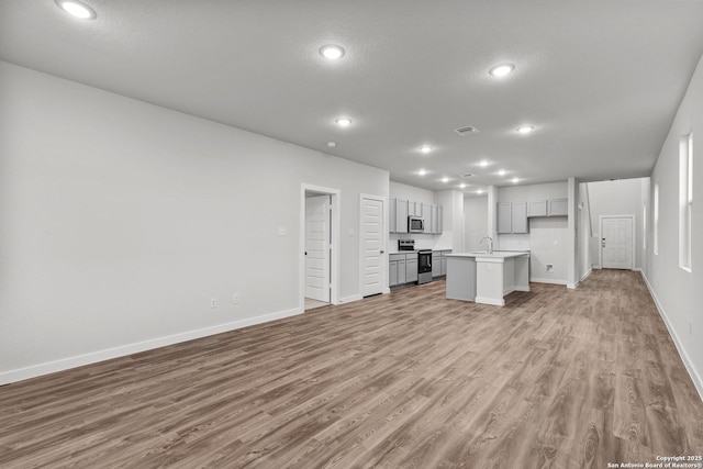 kitchen featuring a kitchen island with sink, visible vents, open floor plan, light countertops, and appliances with stainless steel finishes