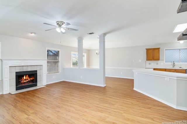 unfurnished living room with light wood-style floors, a sink, visible vents, and ornate columns