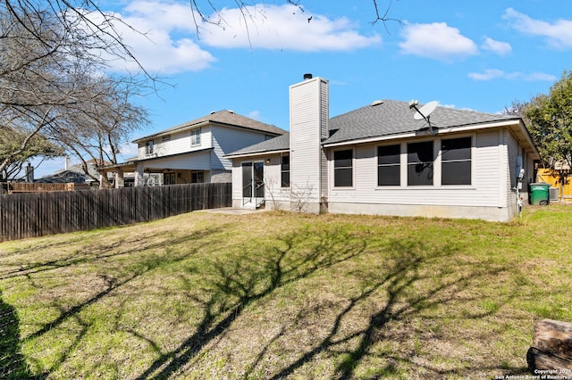 rear view of property featuring a chimney, fence, a lawn, and roof with shingles