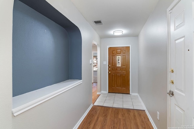 doorway to outside with light wood-type flooring, arched walkways, visible vents, and baseboards