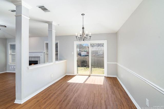 unfurnished dining area featuring wood finished floors, visible vents, baseboards, a tiled fireplace, and decorative columns