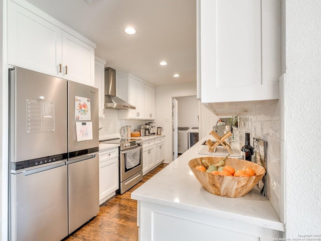 kitchen featuring washer and clothes dryer, appliances with stainless steel finishes, light stone countertops, wall chimney range hood, and white cabinetry