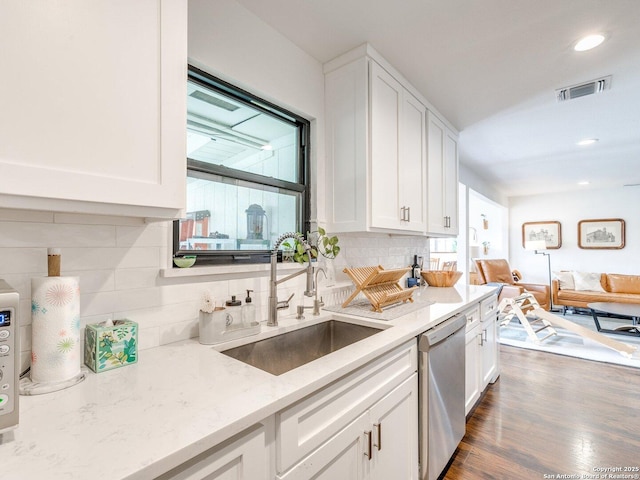 kitchen with tasteful backsplash, white cabinets, light stone countertops, stainless steel dishwasher, and a sink