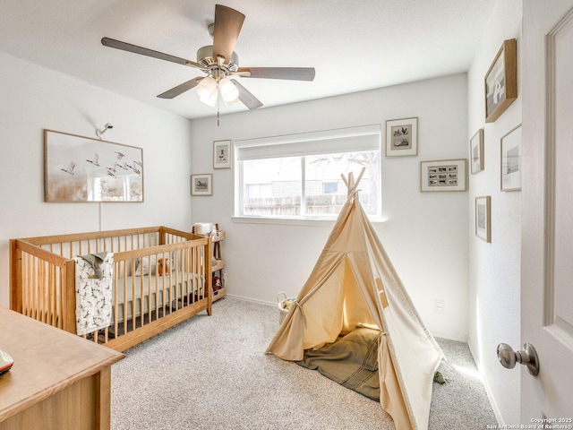 carpeted bedroom featuring a crib, baseboards, and a ceiling fan