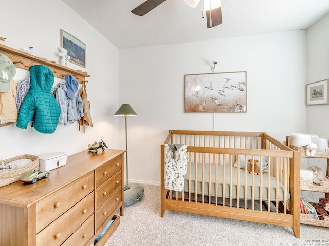 bedroom featuring light carpet, a crib, and a ceiling fan