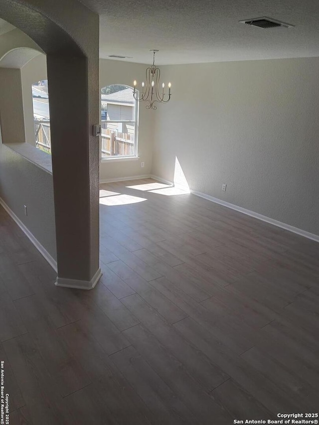 unfurnished dining area with visible vents, dark wood finished floors, arched walkways, and a chandelier