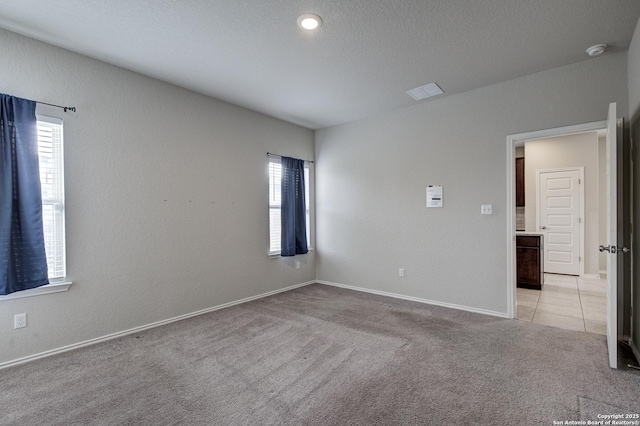 spare room with a textured ceiling, a textured wall, light tile patterned floors, light colored carpet, and baseboards