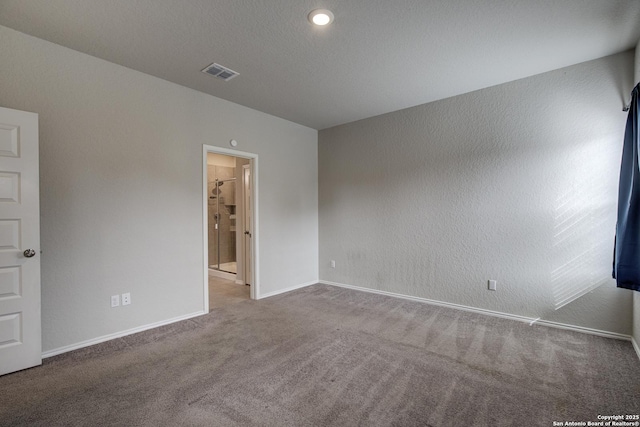 unfurnished room featuring a textured wall, carpet floors, visible vents, and baseboards