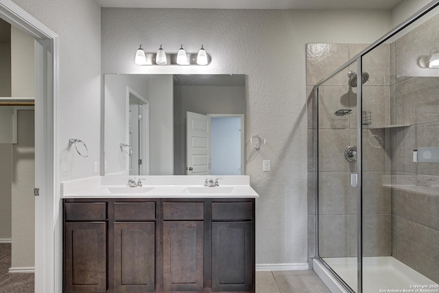 full bath with a sink, double vanity, a shower stall, and a textured wall