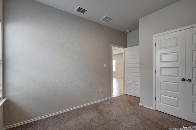 unfurnished bedroom featuring a closet, visible vents, a textured wall, and carpet flooring