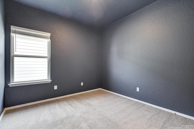 spare room with carpet, a textured wall, and baseboards