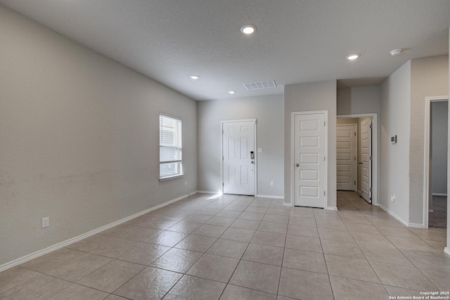 empty room with a textured ceiling, light tile patterned floors, recessed lighting, visible vents, and baseboards