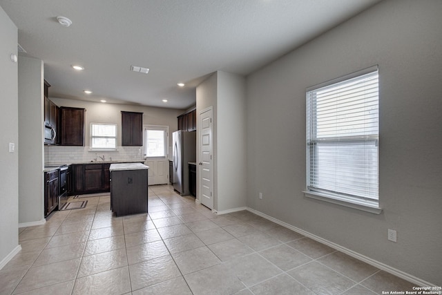 kitchen with light countertops, decorative backsplash, appliances with stainless steel finishes, a kitchen island, and baseboards