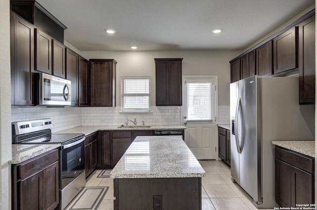 kitchen with a kitchen island, stainless steel appliances, dark brown cabinets, a sink, and light tile patterned flooring