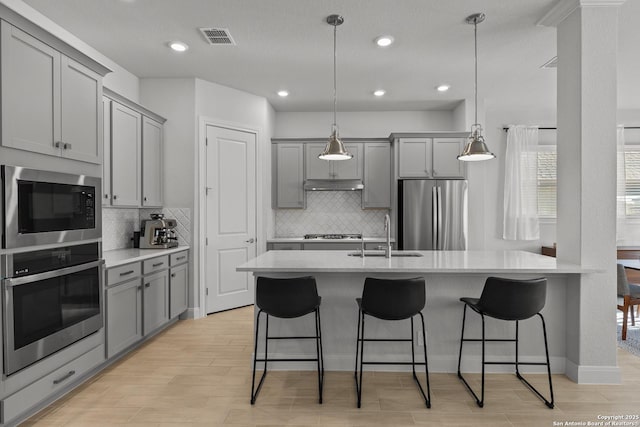 kitchen featuring under cabinet range hood, a sink, light countertops, appliances with stainless steel finishes, and gray cabinets