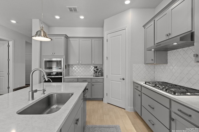 kitchen with decorative light fixtures, light countertops, appliances with stainless steel finishes, a sink, and under cabinet range hood