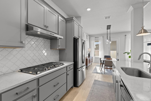 kitchen with under cabinet range hood, stainless steel appliances, a sink, light countertops, and decorative light fixtures